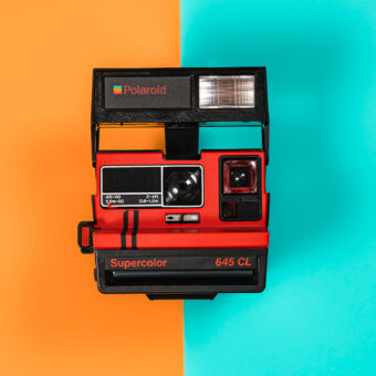 Polaroid Sofortbildkamera vor orange-türkisem Hintergrund