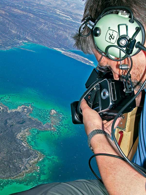 Mann fotografiert mit analoger Kamera aus Helikopter über dem Meer