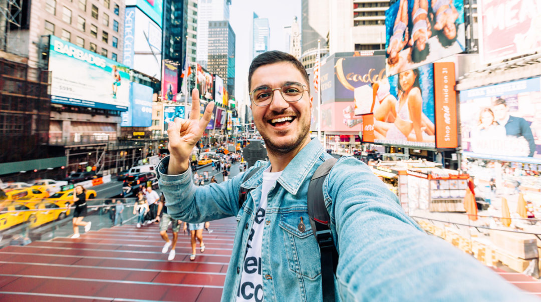 junger fröhlicher Mann macht ein Selfie am Times Square und das Peace-Zeichen in die Kamera