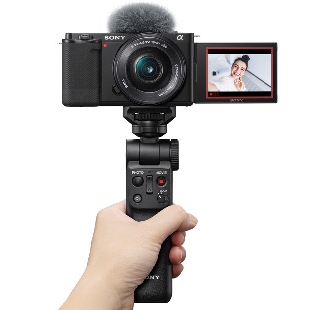 Sony ZV-E10 in der Hand Sony ZV-E10 mit dem optionalen Bluetooth-Griff GP-V2PT2BT: Mit einem Powerzoom-Objektiv – wie dem Kitobjektiv – kann der Fotograf über den Griff zoomen.