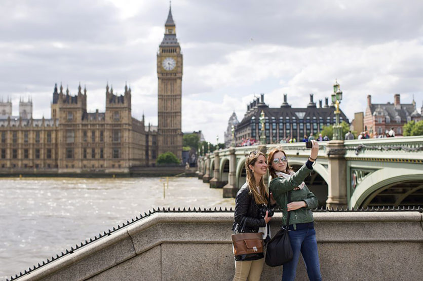 Zwei Frauen stehen an der Themse in London und machen ein Selfe mit dem Big Ben im Hintergrund