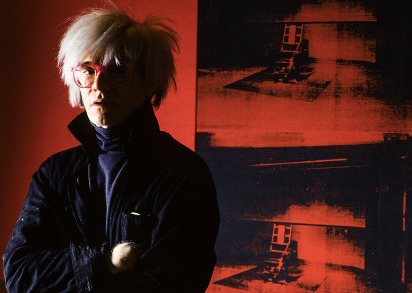 Andy Warhol, posiert vor dem Bild Little Electric Chair
